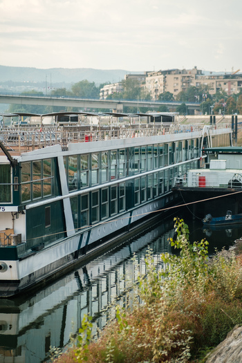 View of a river cruise ship docked on the Danube river with a bridge and city buildings in the background in Novi Sad Vojvodina Serbia. View of a river cruise ship docked on the Danube river with a bridge and city buildings in the background in Novi Sad Vojvodina Serbia.