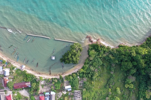 Aerial view of Pulau Maginti featuring wooden boats in turquoise waters near a lush coastline with small houses and dense vegetation in Maginti South East Sulawesi Indonesia.