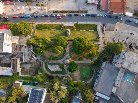 Aerial view of a central park with green trees walking paths and a monument surrounded by urban buildings and a street with parked cars in Kruje Durres County Albania.