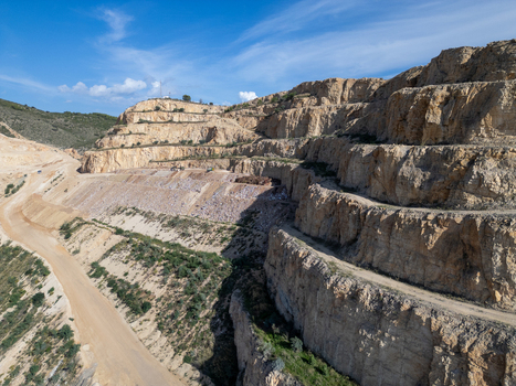 Aerial view of a large open pit quarry with terraced rock faces dirt access roads and exposed stone layers under a clear blue sky in Teulada Valencian Community Spain.