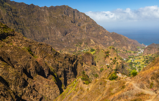 Aerial view of Trilha do Vale do Paul featuring rugged volcanic mountains a lush green valley a winding hiking path and the Atlantic Ocean in Faja de Cima Paul Cabo Verde.