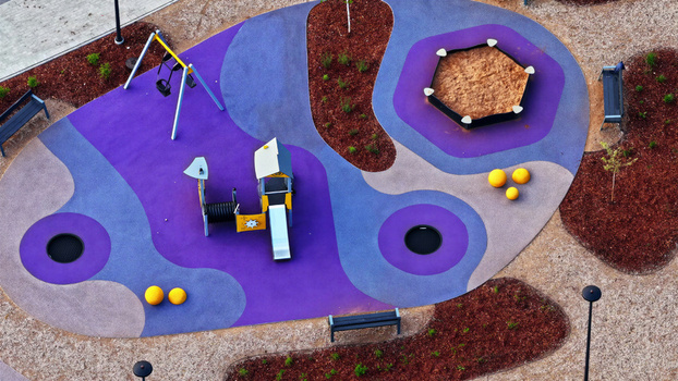 Aerial view of a modern playground with colorful purple and blue rubber flooring a slide swings a sandbox and circular trampolines in Latvija. Aerial view of a modern playground with colorful purple and blue rubber flooring a slide swings a sandbox and circular trampolines in Latvija.
