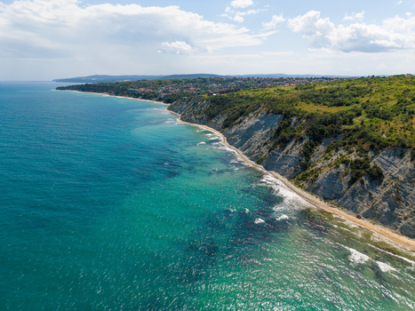 Aerial view of the Byala Cliffs featuring steep white rock formations lush green vegetation and turquoise Black Sea waters under a bright blue sky in Byala Varna Bulgaria. Aerial view of the Byala Cliffs featuring steep white rock formations lush green vegetation and turquoise Black Sea waters under a bright blue sky in Byala Varna Bulgaria.