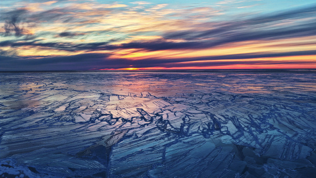 Aerial view of a vast expanse of cracked ice on a frozen lake at sunset with a vibrant colorful sky in Latvia. Aerial view of a vast expanse of cracked ice on a frozen lake at sunset with a vibrant colorful sky in Latvia.