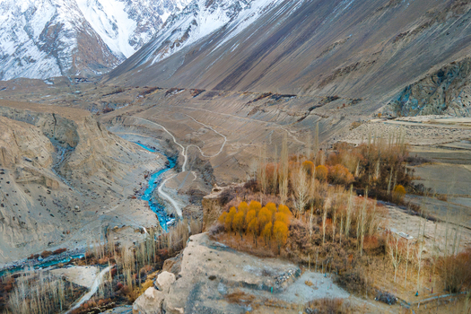 Aerial view of a turquoise river snaking through a rugged valley flanked by golden trees against the backdrop of snow capped mountains Hunza Nagar Gilgit Pakistan. Aerial view of a turquoise river snaking through a rugged valley flanked by golden trees against the backdrop of snow capped mountains Hunza Nagar Gilgit Pakistan.