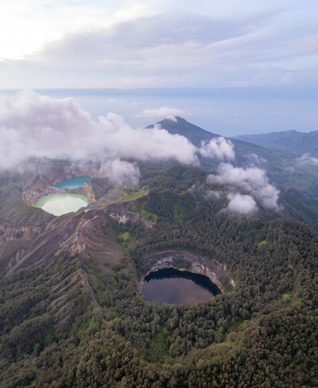 Aerial view of the three colored crater lakes of Kelimutu National Park surrounded by lush volcanic forest and mountain peaks in Detusoko East Nusa Tenggara Indonesia.