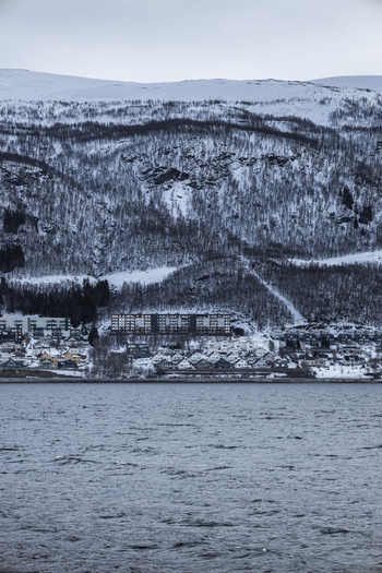 View of residential buildings at the foot of a snow covered mountain across the water in Tromso Troms Norway.