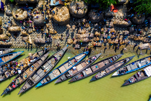 Islampur Bangladesh 05 September 2025 Aerial view of traditional wooden boats docked at a busy riverbank market with workers moving large bundles of jute under bright sunlight. Islampur Bangladesh 05 September 2025 Aerial view of traditional wooden boats docked at a busy riverbank market with workers moving large bundles of jute under bright sunlight.