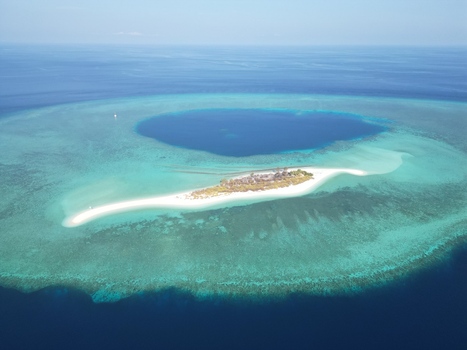 Aerial view of Pulau Ndaa a small island with a white sand beach surrounded by a vibrant turquoise coral reef and deep blue ocean waters in Tomia South East Sulawesi Indonesia.