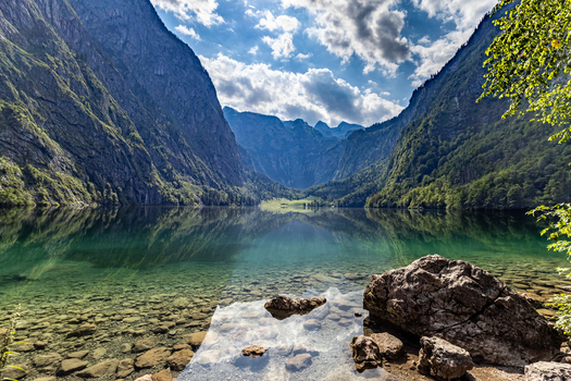 View of Konigssee featuring crystal clear water rocky shoreline and steep mountains Schonau am Konigssee Bavaria Germany.