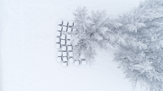 Aerial view of snow covered hay bales arranged in a grid next to frost covered trees in a winter landscape Latvia. Aerial view of snow covered hay bales arranged in a grid next to frost covered trees in a winter landscape Latvia.