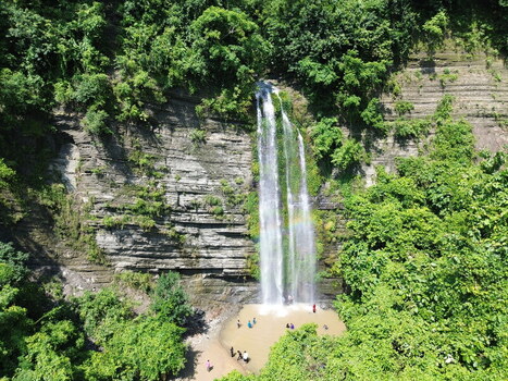 Aerial view of the waterfall in Sitakund surrounded by lush green forest and rocky cliffs with people swimming in the pool at the base. Sitakund Chittagong Division Bangladesh. Aerial view of the waterfall in Sitakund surrounded by lush green forest and rocky cliffs with people swimming in the pool at the base. Sitakund Chittagong Division Bangladesh.