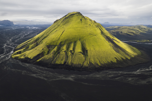 Aerial view of the vibrant green mossy Mælifell volcano rising sharply from the stark black volcanic sands creating a surreal landscape Maelifell Iceland. Aerial view of the vibrant green mossy Mælifell volcano rising sharply from the stark black volcanic sands creating a surreal landscape Maelifell Iceland.