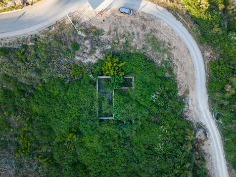 Aerial view of the overgrown stone ruins of an old building surrounded by lush green vegetation next to a winding coastal road Porto Palermo Qarku i Vlores Albania. Aerial view of the overgrown stone ruins of an old building surrounded by lush green vegetation next to a winding coastal road Porto Palermo Qarku i Vlores Albania.