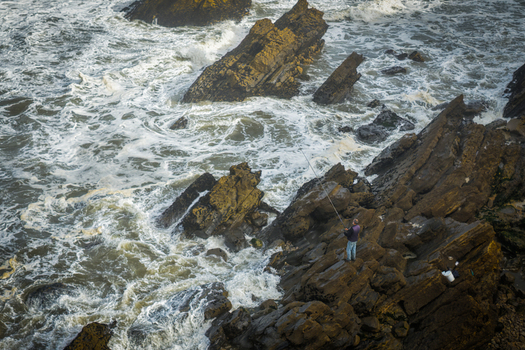 Aerial view of Praia de Sao Pedro de Moel with a fisherman standing on jagged rocks as waves crash against the shore in Marinha Grande Leiria Portugal. Aerial view of Praia de Sao Pedro de Moel with a fisherman standing on jagged rocks as waves crash against the shore in Marinha Grande Leiria Portugal.