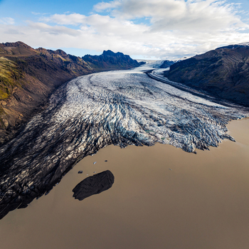 Aerial view of a massive glacier flowing into a glacial lake surrounded by rugged volcanic mountains and dark rocky terrain in Iceland. Aerial view of a massive glacier flowing into a glacial lake surrounded by rugged volcanic mountains and dark rocky terrain in Iceland.