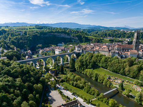 Aerial view of St Nicolas Cathedral and the Zaehringen Bridge spanning the Sarine river valley with historic rooftops and lush green forests in Fribourg Fribourg Switzerland. Aerial view of St Nicolas Cathedral and the Zaehringen Bridge spanning the Sarine river valley with historic rooftops and lush green forests in Fribourg Fribourg Switzerland.