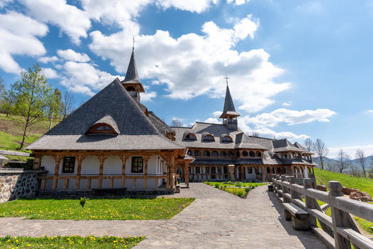 View of a traditional wooden monastery with intricate timber architecture and shingle roofs set against a bright blue sky in Maramures Romania. View of a traditional wooden monastery with intricate timber architecture and shingle roofs set against a bright blue sky in Maramures Romania.