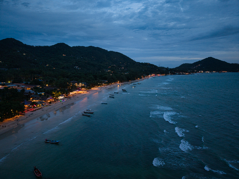 Aerial view of Ko Tao beach at twilight with illuminated buildings small boats anchored in the sea and rolling hills in the background in Ko Tao Surat Thani Thailand.