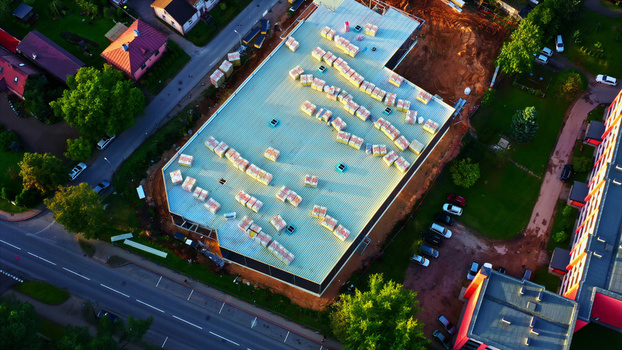 Aerial view of a building under construction with materials stored on the roof surrounded by trees and roads in Latvia. Aerial view of a building under construction with materials stored on the roof surrounded by trees and roads in Latvia.