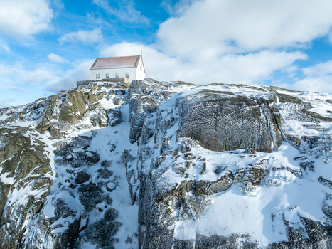Aerial view of a stark white building perched atop a snow dusted rocky peak under a bright scattered sky Lagoa Comprida São Romão Serra da Estrella Portugal. Aerial view of a stark white building perched atop a snow dusted rocky peak under a bright scattered sky Lagoa Comprida São Romão Serra da Estrella Portugal.