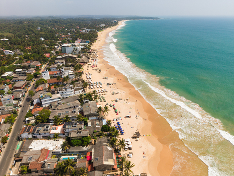Aerial view of Hikkaduwa Beach with turquoise waves golden sand coastal buildings and lush palm trees in Hikkaduwa Southern Province Sri Lanka. Aerial view of Hikkaduwa Beach with turquoise waves golden sand coastal buildings and lush palm trees in Hikkaduwa Southern Province Sri Lanka.