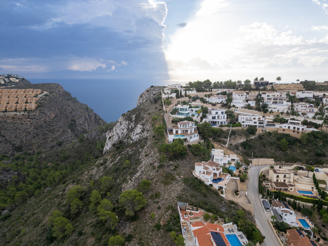 Aerial view of cliffside villas overlooking the Mediterranean Sea with modern architecture swimming pools and dramatic storm clouds in Moraira Valencian Community Spain.