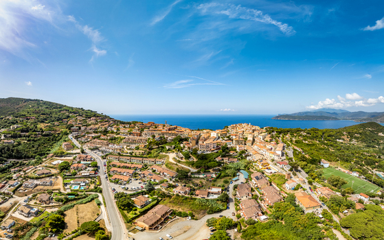 Aerial view of the historic town of Capoliveri nestled on a hillside overlooking the Mediterranean Sea surrounded by lush green landscapes and coastal scenery in Capoliveri Tuscany Italy.