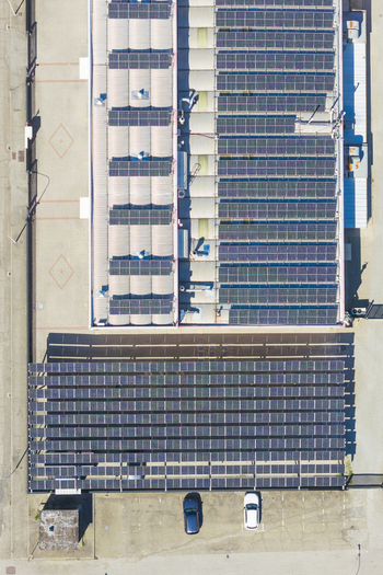 Aerial view of a large industrial building roof covered with extensive solar panel arrays adjacent to a parking lot with two cars in Arezzo Tuscany Italy. Aerial view of a large industrial building roof covered with extensive solar panel arrays adjacent to a parking lot with two cars in Arezzo Tuscany Italy.