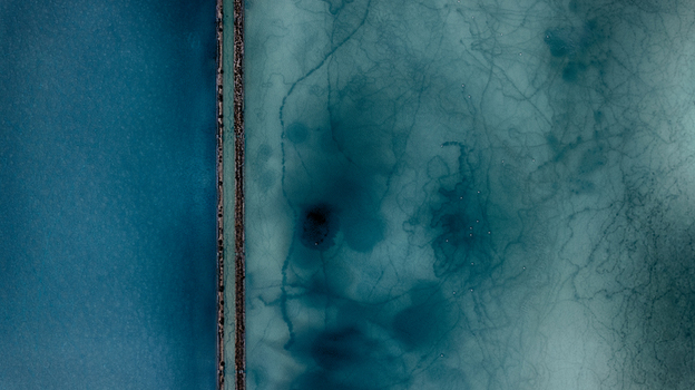 Aerial view of the salt pans with vibrant turquoise water and organic sediment patterns divided by a narrow stone wall in Cagliari Sardinia Italy. Aerial view of the salt pans with vibrant turquoise water and organic sediment patterns divided by a narrow stone wall in Cagliari Sardinia Italy.