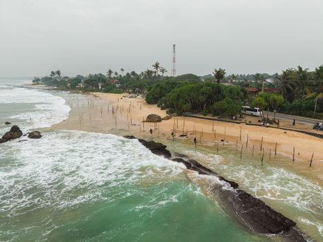 Aerial view of stilt fishermen standing in the ocean near a sandy beach with palm trees and crashing waves in Koggala Southern Province Sri Lanka. Aerial view of stilt fishermen standing in the ocean near a sandy beach with palm trees and crashing waves in Koggala Southern Province Sri Lanka.
