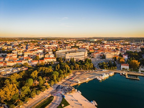 Aerial view of the ancient Roman amphitheater bathed in golden light stands proudly amidst the terracotta rooftops and the deep blue harbor waters Pula Istria County Croatia.