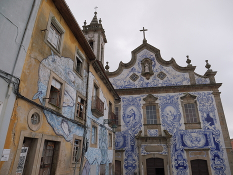 View of the Church of Santa Maria Maior with its intricate blue and white azulejo tiles next to a weathered building featuring a large mural in Covilha Castelo Branco Portugal. View of the Church of Santa Maria Maior with its intricate blue and white azulejo tiles next to a weathered building featuring a large mural in Covilha Castelo Branco Portugal.