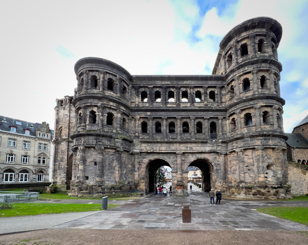 View of the historic Roman city gate Porta Nigra with its weathered stone facade arched gateways and people walking in the square in Trier Rheinland Pfalz Germany.