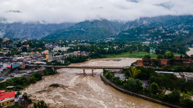 Aerial view of the urban landscape and a wide muddy river with a bridge nestled between lush green mountains and low clouds Muzaffarabad Azad Kashmir Pakistan. Aerial view of the urban landscape and a wide muddy river with a bridge nestled between lush green mountains and low clouds Muzaffarabad Azad Kashmir Pakistan.