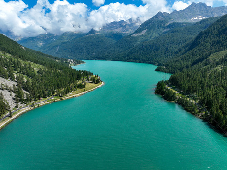 Aerial view of Lago di Ceresole with turquoise water surrounded by lush pine forests and rugged mountain peaks under a cloudy sky Ceresole Reale Piedmont Italy. Aerial view of Lago di Ceresole with turquoise water surrounded by lush pine forests and rugged mountain peaks under a cloudy sky Ceresole Reale Piedmont Italy.