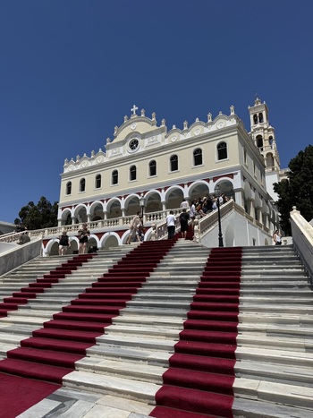 Tinos Greece 21 September 2026 View of Church of Panagia Evangelistria of Tinos with its grand marble staircase covered by a red carpet and people walking up under a clear blue sky.