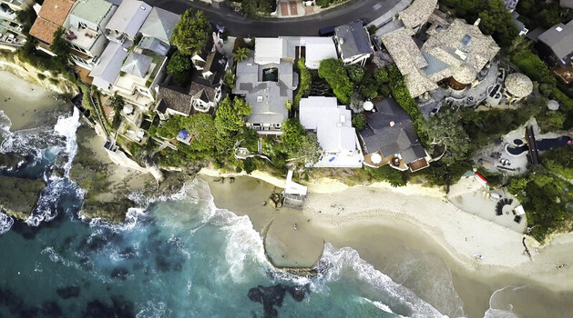Aerial view of Victoria Beach with luxury homes perched on the cliffside overlooking the Pacific Ocean sandy beach and turquoise water in Laguna Beach CA United States.