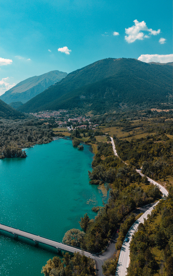 Aerial view of Lago di Barrea with its turquoise waters surrounding mountains lush forests and a bridge crossing the lake in Province of L Aquila Abruzzo Italy.