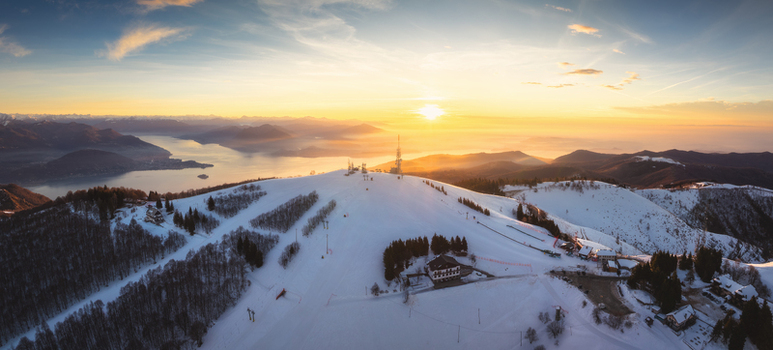 Aerial view of Mottarone mountain ski resort covered in snow during a golden sunrise with Lake Maggiore in the background Mottarone Piedmont Italy. Aerial view of Mottarone mountain ski resort covered in snow during a golden sunrise with Lake Maggiore in the background Mottarone Piedmont Italy.