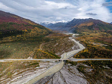 Aerial view of Delta River flowing through a valley with autumn forests snow capped mountains and a highway bridge in Southeast Fairbanks Alaska United States. Aerial view of Delta River flowing through a valley with autumn forests snow capped mountains and a highway bridge in Southeast Fairbanks Alaska United States.