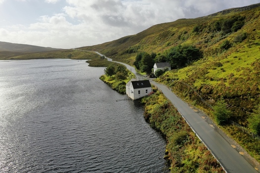 Aerial view of a quiet road running alongside a dark loch with white houses nestled against green hills in Portree Scotland United Kingdom. Aerial view of a quiet road running alongside a dark loch with white houses nestled against green hills in Portree Scotland United Kingdom.