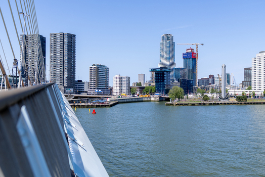 View of the modern Rotterdam skyline with skyscrapers and the Nieuwe Maas river seen from the Erasmus Bridge under a clear blue sky in Rotterdam South Holland Netherlands. View of the modern Rotterdam skyline with skyscrapers and the Nieuwe Maas river seen from the Erasmus Bridge under a clear blue sky in Rotterdam South Holland Netherlands.
