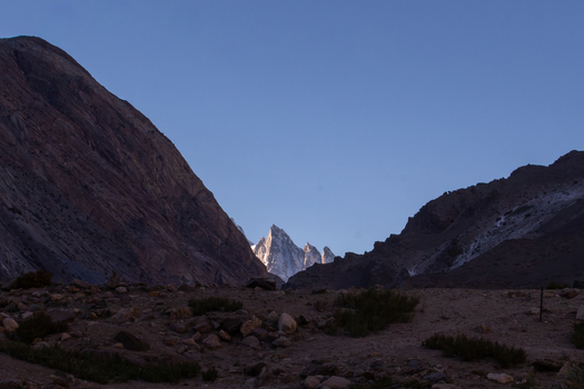 View of the snow capped peak of K2 rising above the rocky terrain and shadows of the Karakoram mountains in Gilgit Baltistan Pakistan. View of the snow capped peak of K2 rising above the rocky terrain and shadows of the Karakoram mountains in Gilgit Baltistan Pakistan.