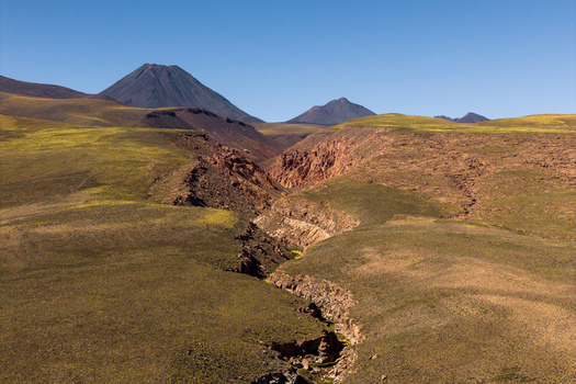 Aerial view of Chiliques volcano rising above the arid Atacama Desert landscape with deep rocky ravines and sparse vegetation in San Pedro de Atacama Antofagasta Chile. Aerial view of Chiliques volcano rising above the arid Atacama Desert landscape with deep rocky ravines and sparse vegetation in San Pedro de Atacama Antofagasta Chile.