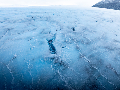 Aerial view of Breidamerkurjokull glacier with deep blue crevasses and a small group of people walking on the ice in Sveitarfelagid Hornafjordur Iceland. Aerial view of Breidamerkurjokull glacier with deep blue crevasses and a small group of people walking on the ice in Sveitarfelagid Hornafjordur Iceland.