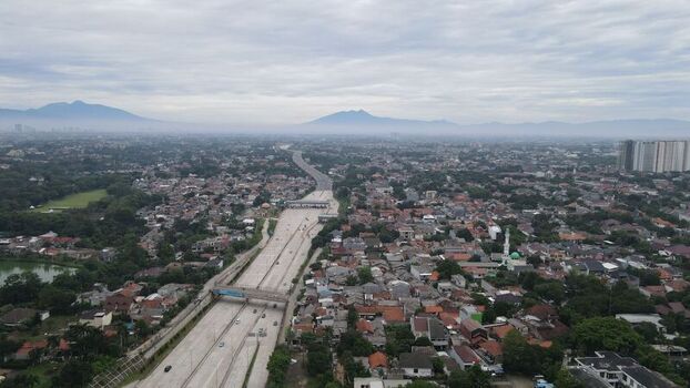 Aerial view of Jalan Tol Depok Antasari highway cutting through the urban landscape with residential rooftops and distant mountains Kecamatan Cilandak Daerah Khusus Ibukota Indonesia. Aerial view of Jalan Tol Depok Antasari highway cutting through the urban landscape with residential rooftops and distant mountains Kecamatan Cilandak Daerah Khusus Ibukota Indonesia.