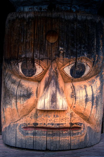 View of a detailed carved wooden totem pole face with weathered textures and painted features at Ksan Campground in Ksan British Columbia Canada. View of a detailed carved wooden totem pole face with weathered textures and painted features at Ksan Campground in Ksan British Columbia Canada.