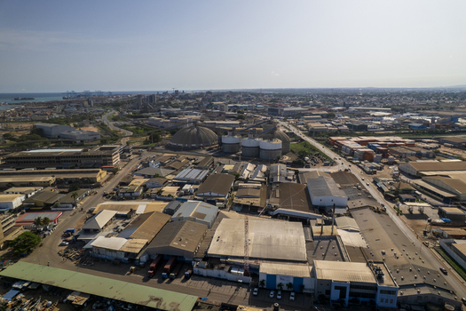 Aerial view of industrial buildings and road networks sprawl contrasting sharply with the distant sea under a hazy sky Tema Ghana. Aerial view of industrial buildings and road networks sprawl contrasting sharply with the distant sea under a hazy sky Tema Ghana.