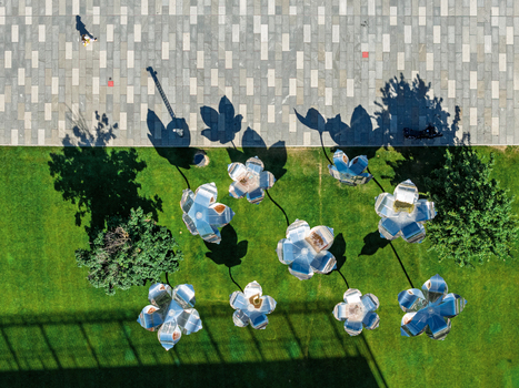 Aerial view of metallic flower sculptures on a green lawn with long shadows and a person walking on the adjacent paved walkway in Belgrade City of Belgrade Serbia. Aerial view of metallic flower sculptures on a green lawn with long shadows and a person walking on the adjacent paved walkway in Belgrade City of Belgrade Serbia.